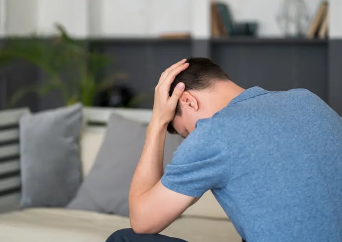 Mann sitzt auf Couch und hält sich den Kopf