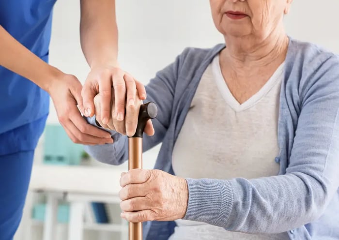 Älterer Dame wird beim Aufstehen von Pflegerin unterstützt