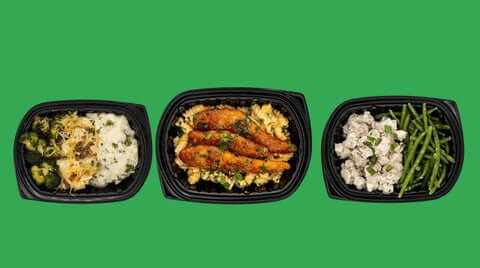 Already cooked meal delivery showcasing a variety trio of prepared meals (broccoli & mash, chicken pasta, chicken & green beans) on a clean green background.