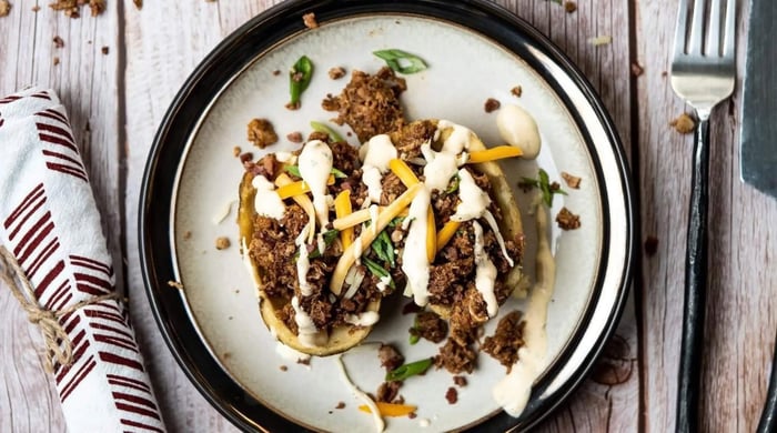 Balanced prepared meal portions with stuffed potato skins topped with beef, cheese, and creamy sauce on a plate.