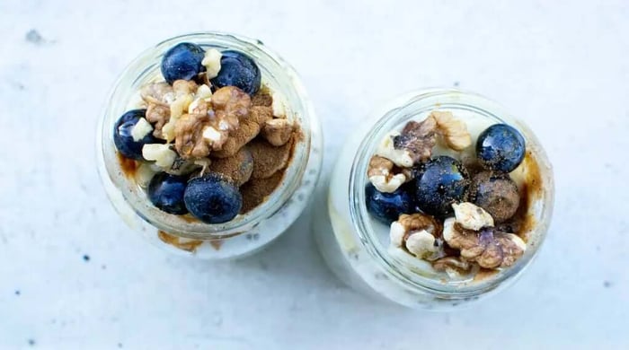Blueberry overnight oats topped with fresh blueberries, walnuts, and cinnamon served in two glass mason jars.