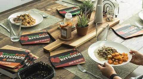Convenient meal plans pictured as a family-style table setting with plated meals and Clean Eatz Kitchen grab-n-go branding.