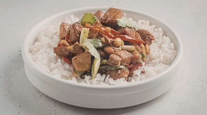 Easy asian chicken and brown rice recipe featuring soy-glazed chicken pieces with peppers, peanuts, and cilantro served over steamed white rice in a shallow bowl.