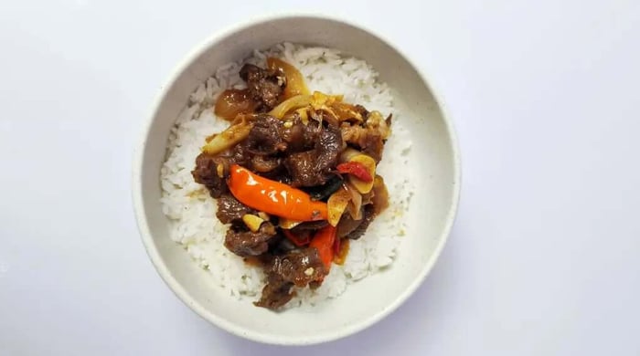 Barbacoa beef bowl with braised beef, fried egg, kimchi rice, sesame seeds, and shredded scallions in a dark bowl.