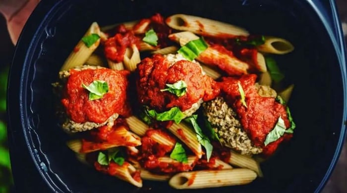 Fully prepared meal of pasta with meatballs, marinara sauce, and basil in a black bowl.