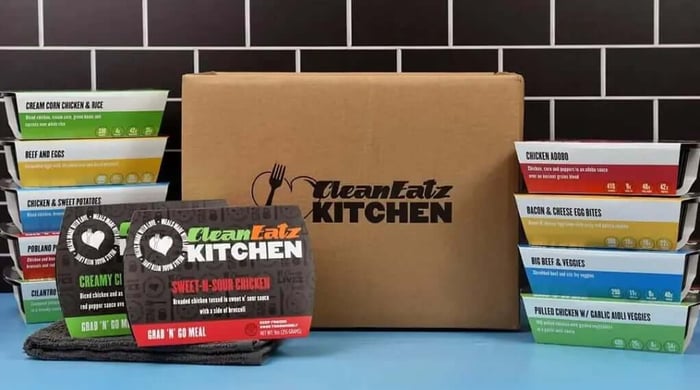 Gluten-free meal plan delivery box from CleanEatz Kitchen with assorted packaged meals on blue counter.