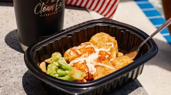 Gourmet gluten-free meals in a takeout tray with broccoli, pasta, and chicken beside a CleanEatz cup.