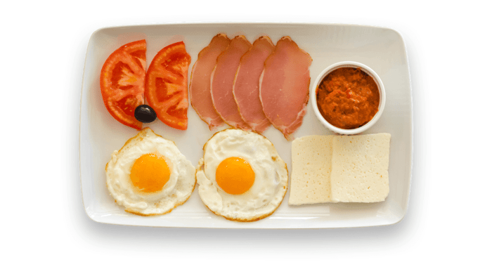 Healthy breakfast ideas featuring two sunny-side-up eggs, sliced ham, tomato wedges, white cheese, and a side of tomato relish on a white rectangular plate.