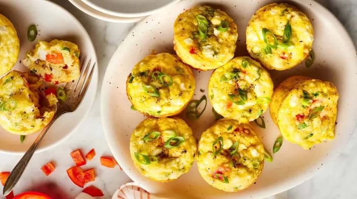 Healthy egg muffin cups recipe featuring golden baked egg cups with red pepper, scallions, and feta arranged on a plate with diced peppers on the side.