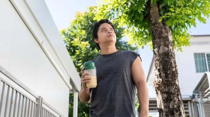 Healthy protein shake being carried by a fit young man in a sleeveless shirt outdoors after a workout.
