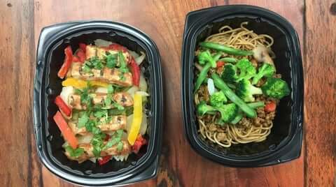 Healthy meal plans delivered featuring fresh, portioned meals in black containers (chicken and veggies; noodles with broccoli) ready to heat and eat.