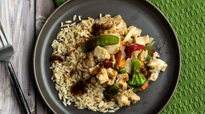 Healthy meal prep ideas featuring chicken, rice, and mixed vegetables with savory sauce in a black bowl.