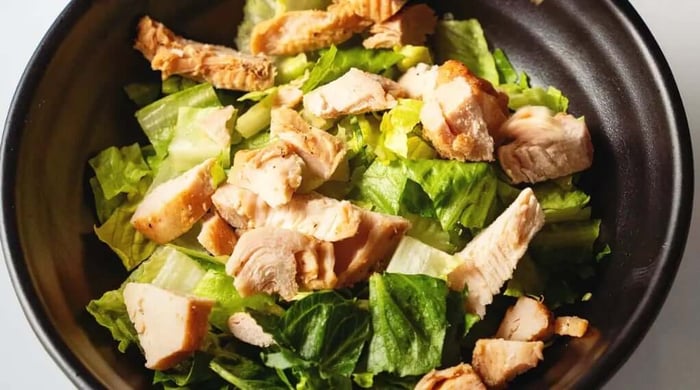 Healthy prepared meal featuring sliced grilled chicken over fresh romaine lettuce in a simple black bowl