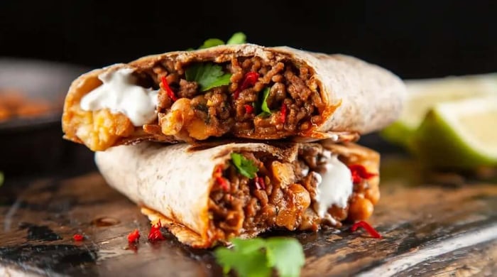 High protein burrito stacked and cut open revealing seasoned ground beef, chickpeas, red chili, cilantro, and sour cream in a whole wheat tortilla.