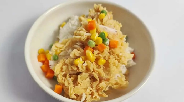High protein chicken bowl with shredded egg-drop chicken over white rice topped with sweet corn, green peas, and diced carrots in a cream bowl.