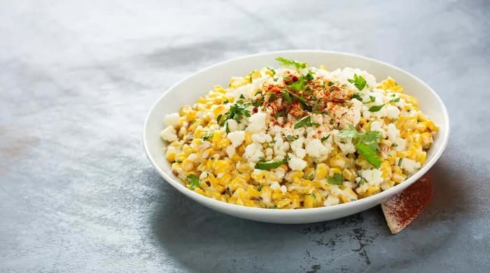 High protein food served as creamy Mexican street corn salad topped with crumbled cotija cheese, fresh cilantro, and smoked paprika in a white bowl.