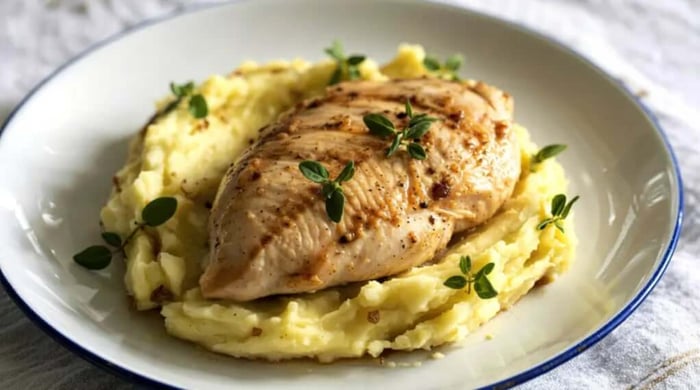 High protein food with a seasoned grilled chicken breast resting on creamy mashed potatoes garnished with fresh thyme in a blue-rimmed bowl.