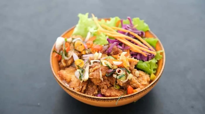 High protein food served as a crispy fried chicken bowl topped with pickled vegetables, shredded purple cabbage, carrots, and fresh lettuce in a rustic clay bowl.