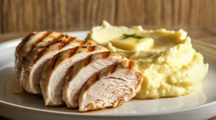 High protein mashed potato served alongside sliced grilled chicken breast with butter on a white plate.