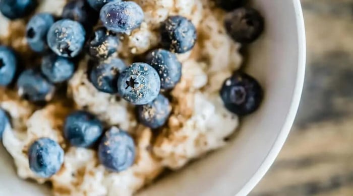 High protein meal prep of creamy blueberry oatmeal topped with fresh blueberries and flaxseed in a white bowl.