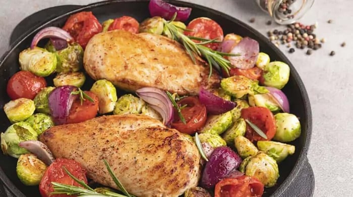 High protein meals with two seared chicken breasts roasted in a cast iron skillet alongside Brussels sprouts, cherry tomatoes, and red onions with fresh rosemary.