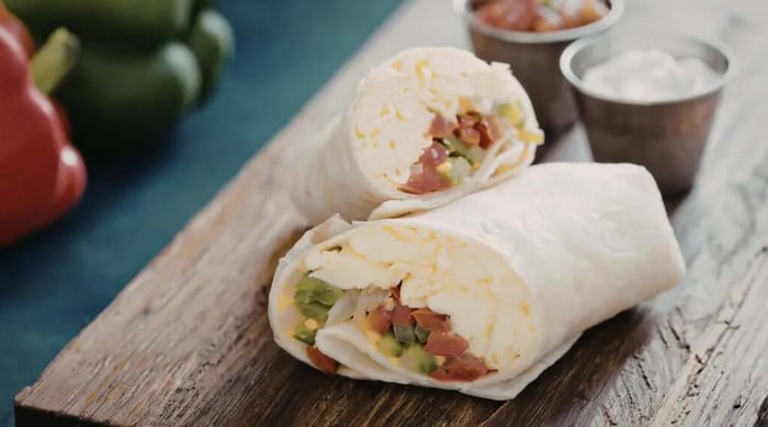 High protein meals with a flour tortilla burrito cut in half and filled with shredded chicken, cheddar cheese, bacon, and diced vegetables served with salsa and sour cream.