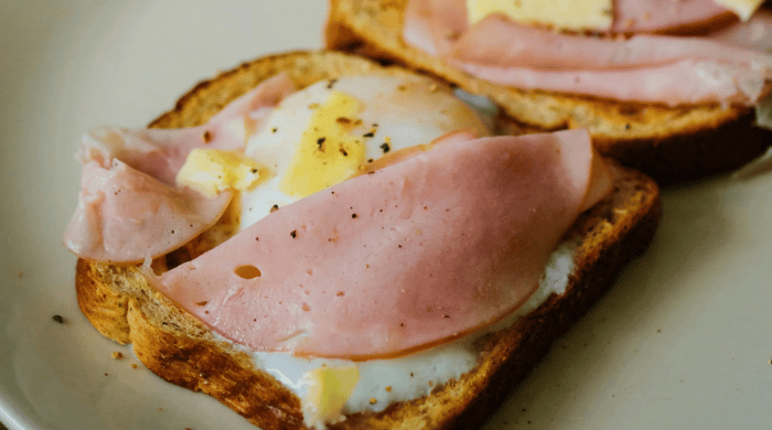 High protein meals with sliced ham layered over a fried egg on toasted sourdough bread seasoned with black pepper.