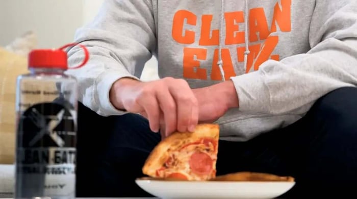 High-protein diet meal lifestyle image showing Clean Eatz customer enjoying a protein-focused slice of pizza with branded drink