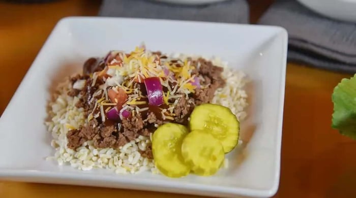 High-protein meal prep bowl with seasoned ground beef, brown rice, shredded cheese, onions, and sliced pickles