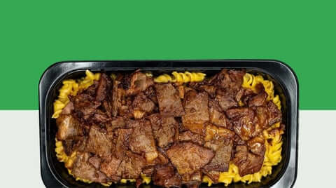 High-protein meal prep featuring a close-up black meal tray topped with sliced beef over cheesy pasta on a green background.