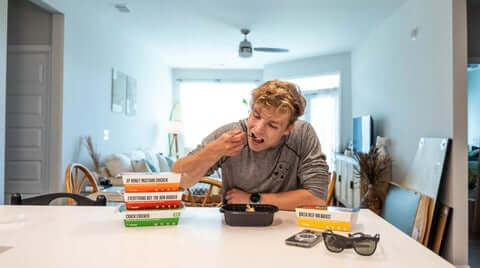 Meal ideas for the week showing a person eating at home with multiple stacked ready-made meals nearby for easy grab-and-go variety.
