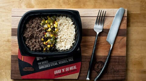 Nutritious frozen meals displayed as shredded steak, vegetables, and rice meal with balanced macros on wooden board.
