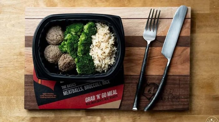 Portion control meal prep tray with meatballs, broccoli, and rice on wooden board with fork and knife.