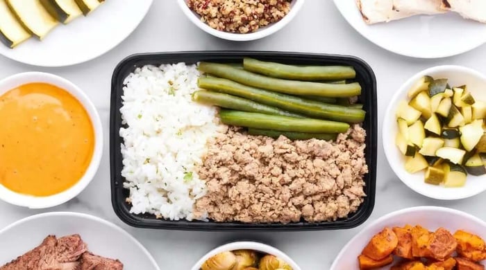 Portion-controlled meal of ground turkey, green beans, and white rice in a black container surrounded by build-your-own ingredient bowls.