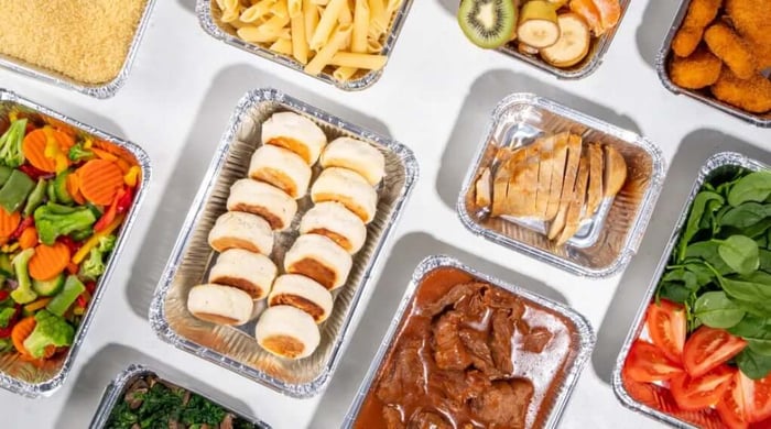 Ready-to-eat trays featuring couscous, penne pasta, fresh fruit, chicken nuggets, roasted vegetables, sliced turkey, beef stew, and spinach with tomatoes from a healthy meal delivery service.