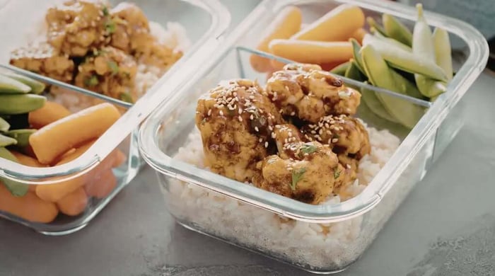 Sesame teriyaki chicken over white rice with baby carrots and snap peas in glass containers from a healthy meal delivery service.