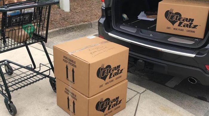 Weight loss meal plans delivery with Clean Eatz branded boxes of prepared meals beside a car trunk ready for pickup or transport.