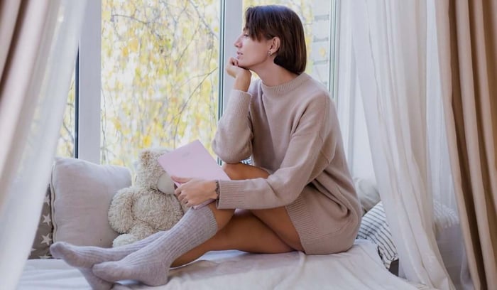 Pensive woman with pink notebook sitting by a window