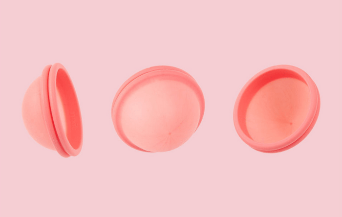 Three pink reusable menstrual discs shown from different angles