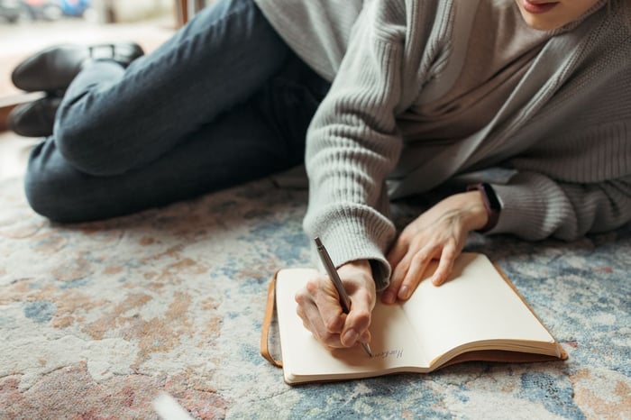 Person lying on the floor writing notes in a journal