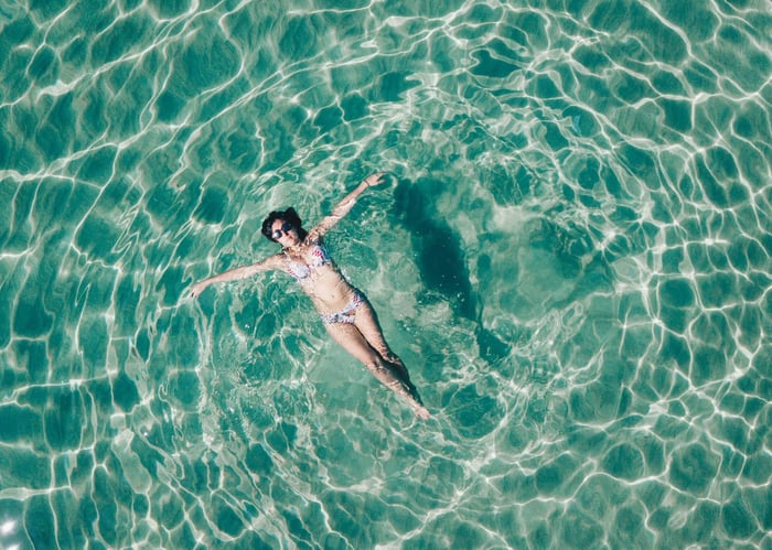 Woman in bikini leisurely floating in a sunlit pool.