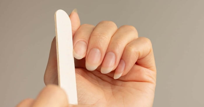 A close-up view shows a person with long nails holding a white nail file up to their index finger nail.