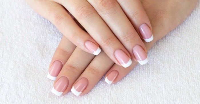 A close-up view shows one hand on top of the other on top of a white cloth. The nails have classic French tips.