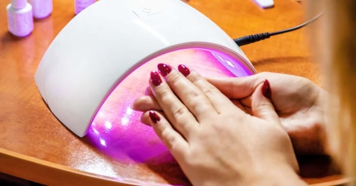 An over-the-shoulder view shows a woman observing the freshly cured gel manicure on her nails. Her nails are fuchsia.