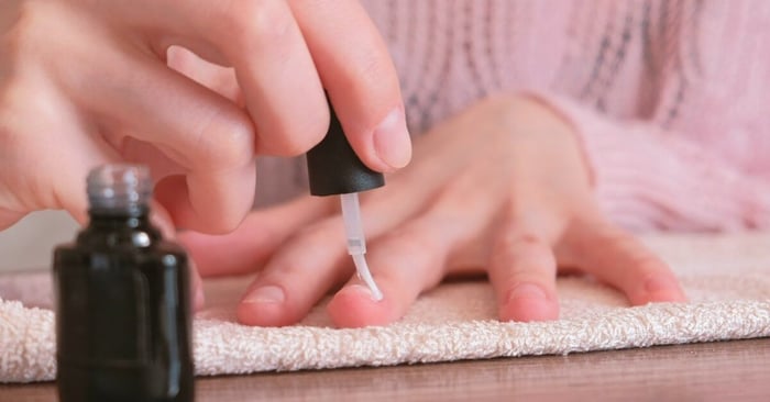 A close-up view of a black gloved hand holding the finger of another person; the other gloved hand holds a nail brush.