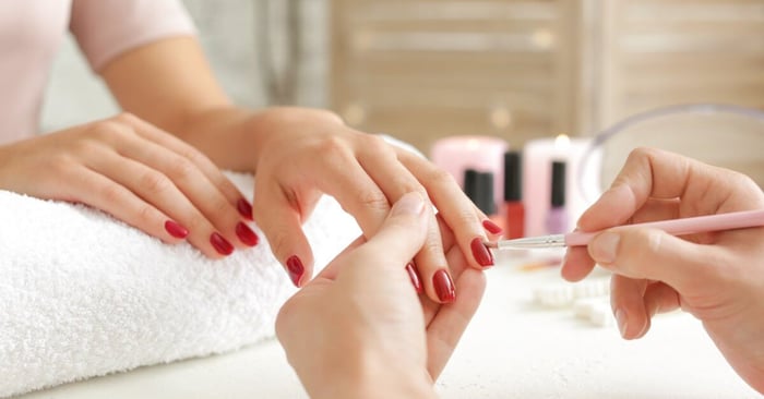 A person holds out one hand as the other rests on a towel; someone else holds a brush to apply red polish to the nail.