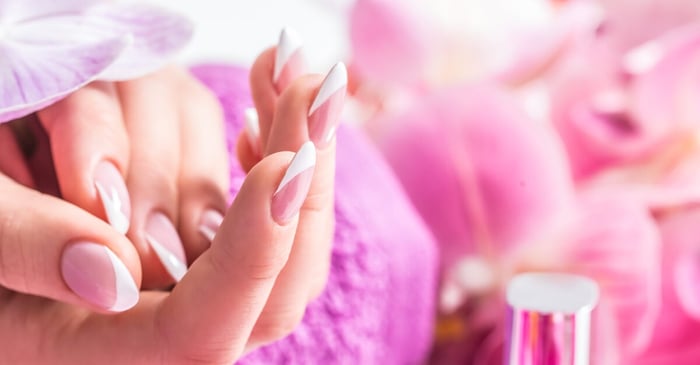 A close-up of a beautiful nail manicure with decoration from pink and purple orchids in the background.