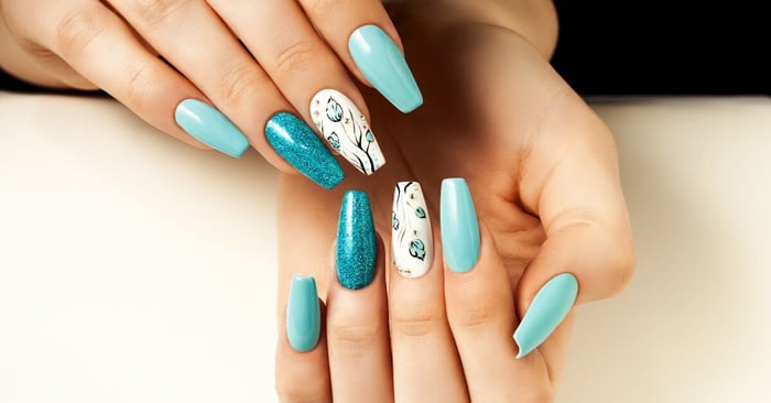 Manicured nails where several nails are light blue, the middle nail has a floral design, and the ring fingernail is glittery.