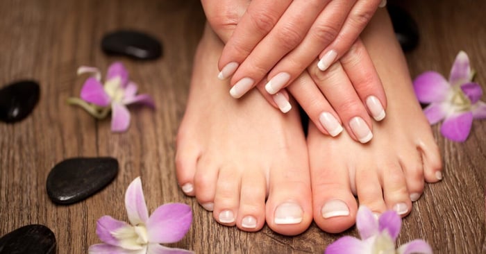 A close-up of someone's manicure and pedicure. Their nails are french tips and there are flowers and rocks surrounding them.