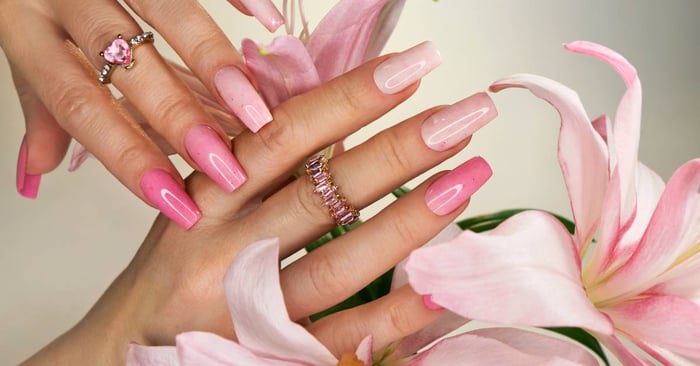 Long gel pink nails with glitter. The model is wearing matching pink rings; one is a heart, and the other a band.